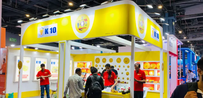 K-10 exhibition stall with yellow and white branding, illuminated displays and overhead fascia